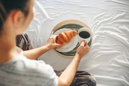 Girl drinks morning delicious coffee with a croissant in bed.