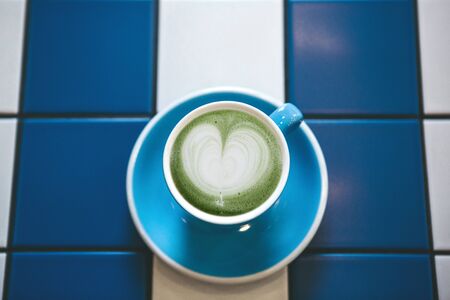 Closeup fresh fragrant healthy green Matcha latte tea in a blue mug on a table of blue and white...