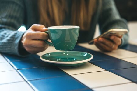 A girl drinks hot tea or coffee in a cafe and uses a cell phone or mobile phone.の写真素材