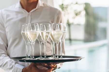 The waiter is holding a tray with glasses of champagne or white sparkling wine. Service in the restaurant.の写真素材