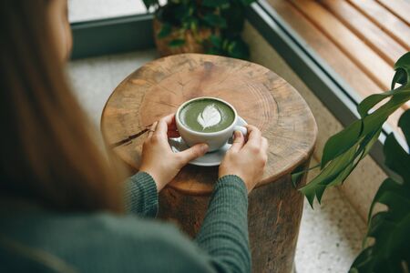 Girl drinks aromatic fresh and healthy green matcha latte tea in a cafe.の写真素材