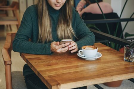 The girl uses a cell phone and drinks coffee. She has a meeting or she drinks a morning cappuccino...
