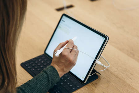 Turkey, Istanbul, December 17, 2019: sale New tablet APPLE iPad in the official Apple store. The buyer is trying to draw a simple drawing with the stylus on the gadget screen.のeditorial素材