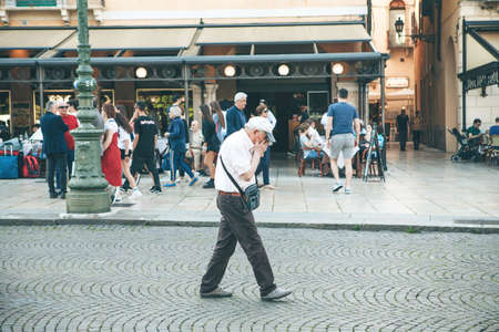 Italy, Verona, June 01, 2019: An elderly man covers his face with his hands in a crowded place or he coughs or sneezes.のeditorial素材