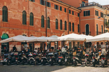 Italy, Verona, June 01, 2019: View of a street restaurant or cafe or pizzeria with many people and visitors. Nearby are motorcycles.のeditorial素材
