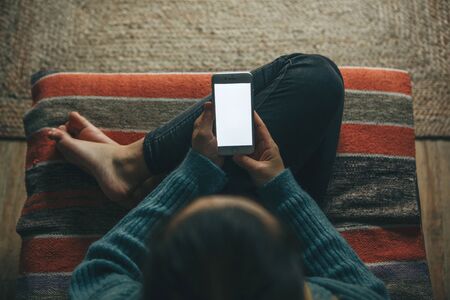 Girl at home uses a cell phone or mobile phone mockup. Modern technology in everyday life.の写真素材