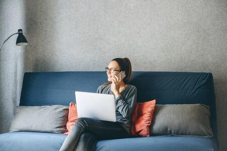 A girl works from home or a student is studying from home or a freelancer. She uses a laptop and a phone.の写真素材