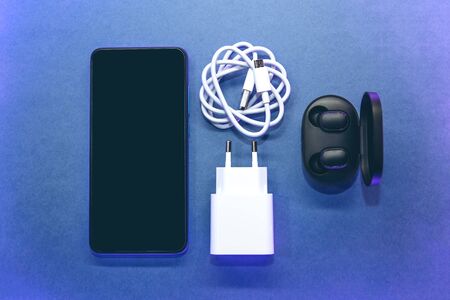 Set of cell phone, wireless headphones and charger on a blue background.の写真素材