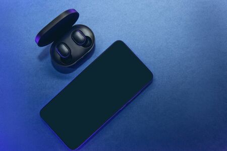 The wireless headphones in the box are unpacked and the cell phone on a classic blue background.の写真素材