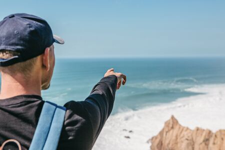 Tourist shows his hand into the distance at the ocean or seaの写真素材