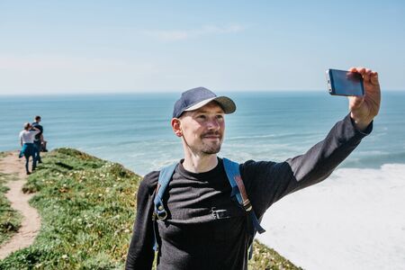 A tourist photographs a beautiful landscape or takes a selfie against the background of the Atlantic Ocean in Portugal.の写真素材