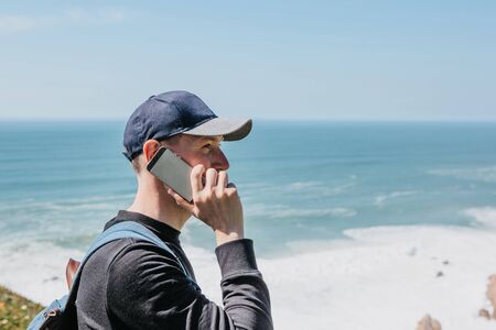 Tourist or student talking on a cell phone or mobile phone on the background of the oceanの写真素材