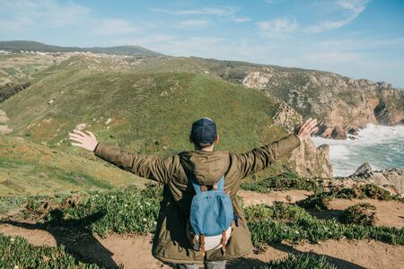 A tourist with a backpack outdoors raised his hands up and shows how happy he is and how free.の写真素材