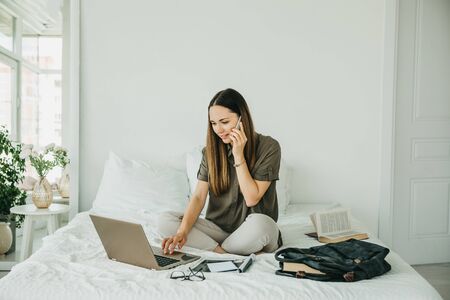 Young beautiful girl or student uses a laptop and cell phone or mobile phone at home.の写真素材