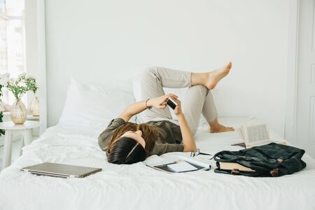 A girl student or schoolgirl lies in bed and uses a cell phone at home after class.の写真素材