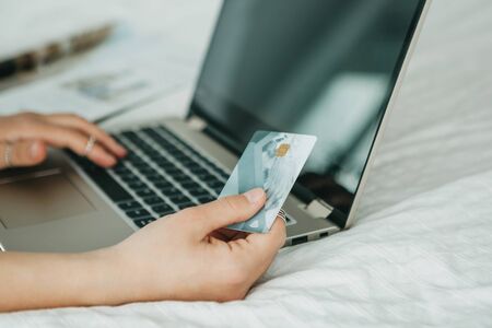 A girl holds a credit card or bank card in her hand next to a laptop. Online shopping concept.の写真素材