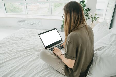 Girl at home uses laptop mockup. Modern technology in everyday life. Blank white screen place for text or template.の写真素材