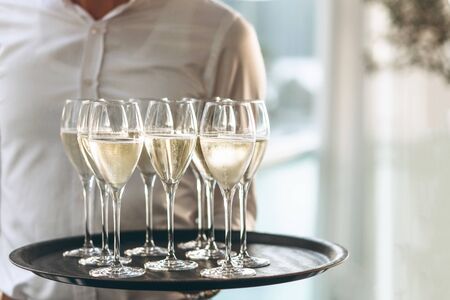 The waiter is holding a tray with glasses of champagne or white sparkling wine. Service in the...