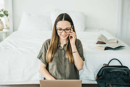 Young beautiful girl or student uses a laptop and cell phone or mobile phone at home.の写真素材