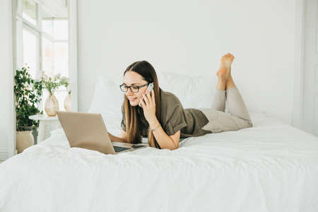 Young beautiful girl or student uses a laptop and cell phone or mobile phone at home.の写真素材