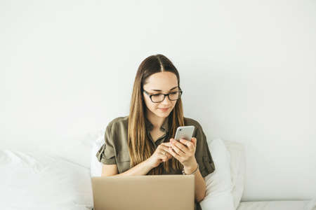 Young beautiful girl or student uses a laptop and cell phone or mobile phone at home.の写真素材