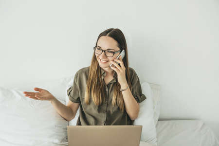 Young beautiful girl or student uses a laptop and cell phone or mobile phone at home.の写真素材