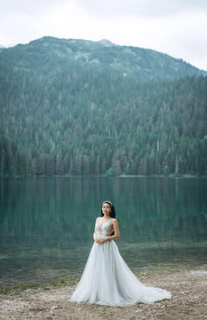 Portrait of a beautiful elegant bride in a white traditional dress on a lake backgroundの写真素材