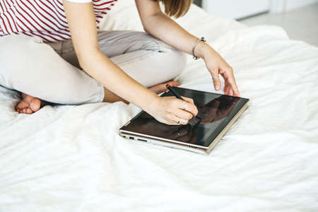 Girl digital artist draws with a stylus on a tablet or laptop. She is a student and is studying drawing or is this her professional occupation.の写真素材