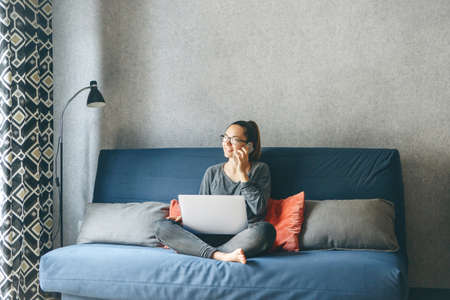 A girl works from home or a student is studying from home or a freelancer. She uses a laptop and a phone.の写真素材