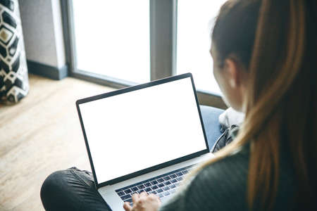 Girl at home uses laptop mockup. Modern technology in everyday life. Blank white screen place for text or template.の写真素材