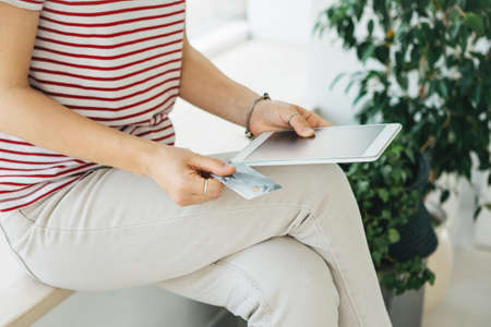 A girl holds a credit card or bank card in her hand next to a tablet. Online shopping concept.の写真素材