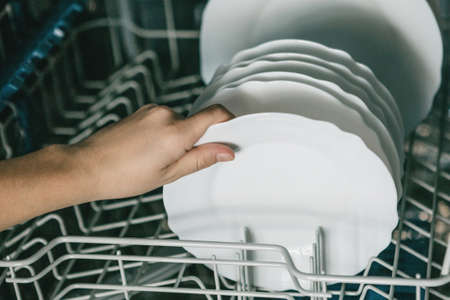 Closeup female hand with a plate. A woman puts a plate in the dishwasher or takes a plate from it. Housewife does her housework.の写真素材