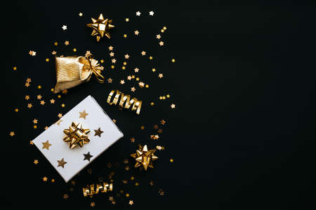 Gift box and various golden items on a black or dark background. Festive conceptual Christmas or New Year background or Black Friday sale. Nearby copy space.の写真素材