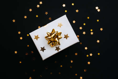 Festive gift box with gold stars and bow on a black background.の写真素材