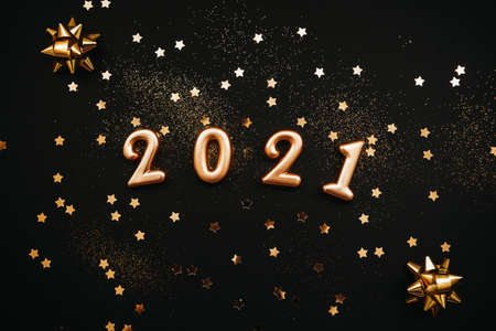 Gold numbers 2021 and golden confetti on dark or black background. Christmas or New Year background.の写真素材
