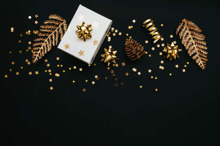Gift box and various golden items on a black or dark background. Festive conceptual Christmas or New Year background or Black Friday sale. Copy space below.の写真素材