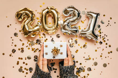 The girl holds a box with a gift in her hands. Nearby confetti and gold and silver numbers 2021. Festive New Year and Christmas concept background.の写真素材