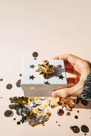 Person holds in hand a box with a gift on a pink background with confetti.の写真素材
