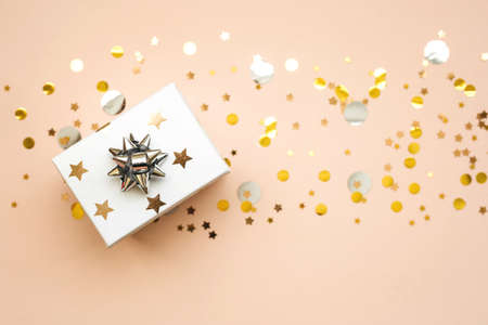 Box with a gift on a pink background with golden and silver confetti. Festive background.