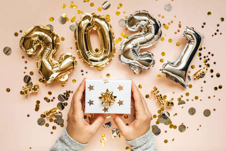 The girl holds a box with a gift in her hands. Nearby confetti and gold and silver numbers 2021. Festive New Year and Christmas concept background.の写真素材