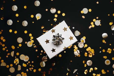 Box with a gift and a lot of confetti on a black background. Festive Christmas or New Year or other holiday concept background.の写真素材