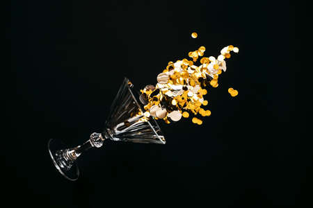 Wine glass with gold sparkles or confetti on a black background. Celebration concept.の写真素材