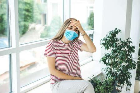 Girl with a medical mask on her face. She has a headache or fever.の写真素材