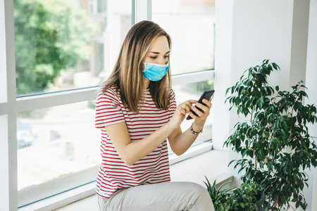 A girl in a protective medical mask uses a cell phone.の写真素材