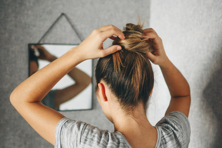 Girl does hairstyle or hair style in front of a mirror in the roomの写真素材