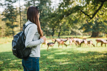 Young beautiful travel girl with backpack looking at wild reindeer grazing in the distanceの写真素材