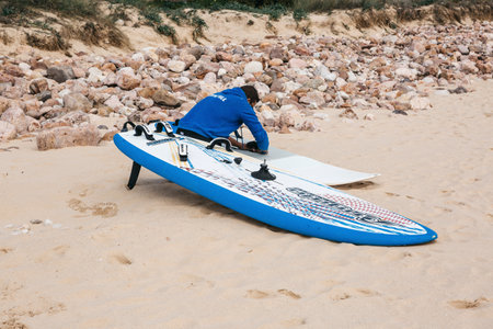 Portugal, Sintra, May 29, 2019: Surfer repairs a surfboard on the beach.のeditorial素材
