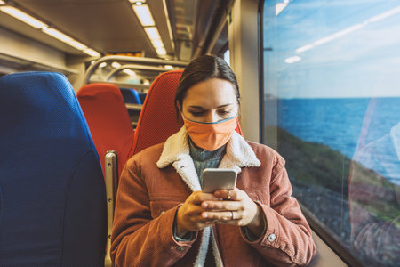 A girl in a protective face mask on the train uses a cell phone. Traveling by train or commuter travel.の写真素材