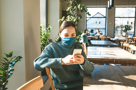 A girl in a protective mask uses a cell phone. Social distancing during a pandemic.の写真素材