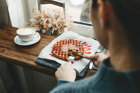The girl cuts a waffle with chocolate and fruit syrup and is going to eat.の写真素材